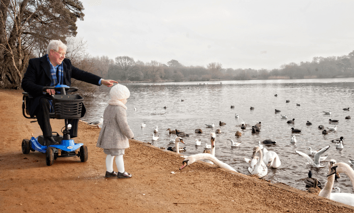 a man with his granddaughter on a mobility scooter by a lake